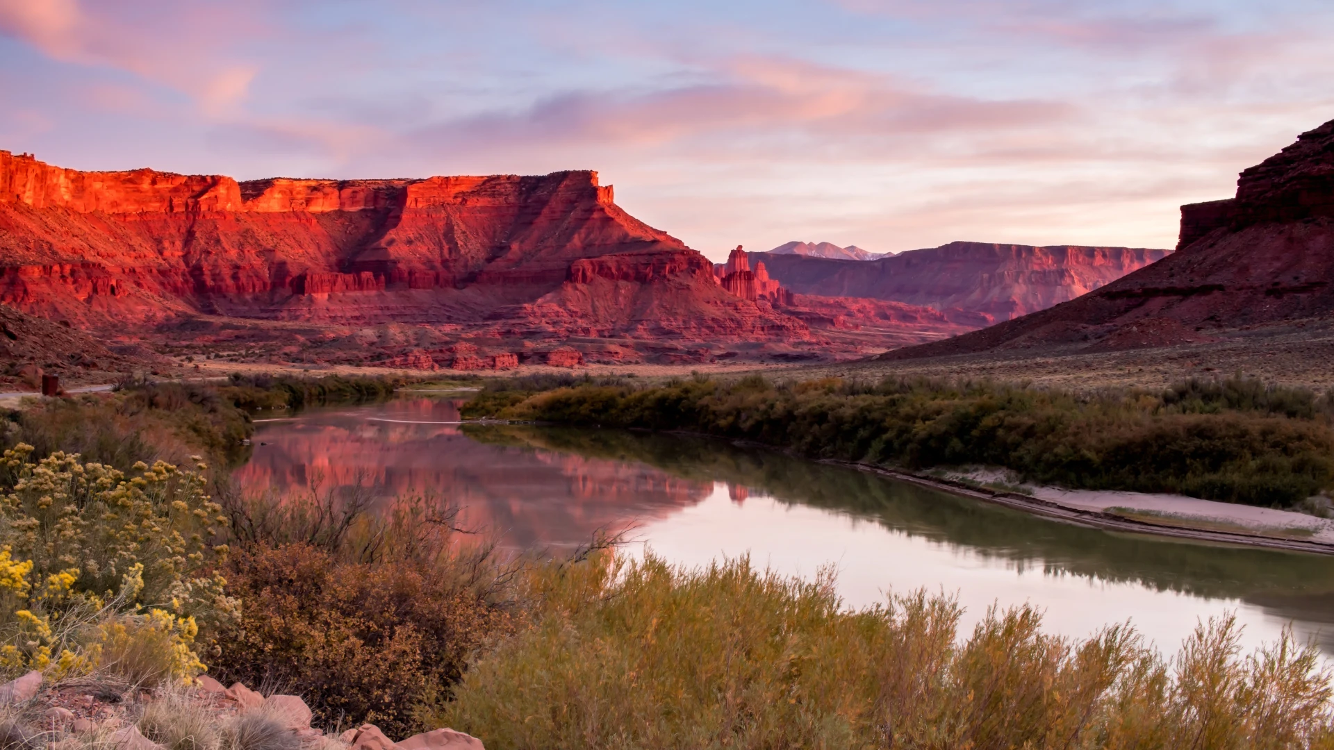 River winding through a desert canyon at sunset with red cliffs and pink sky.