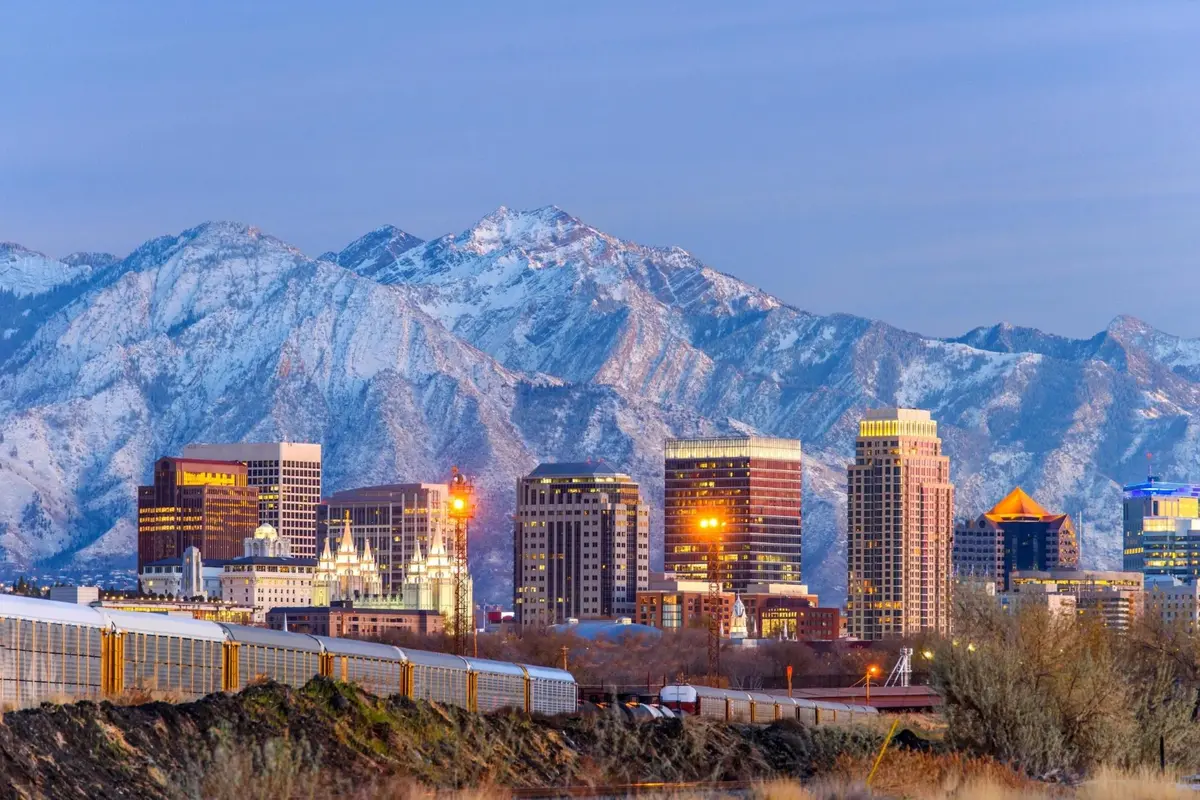Downtown city buildings with snowy mountains in the background at dusk.